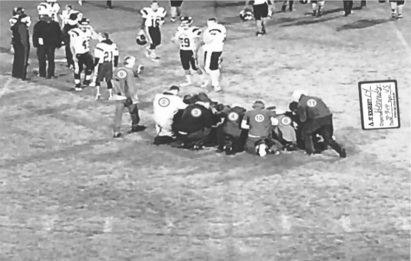 Football players in prayer circle with identification markers on backs